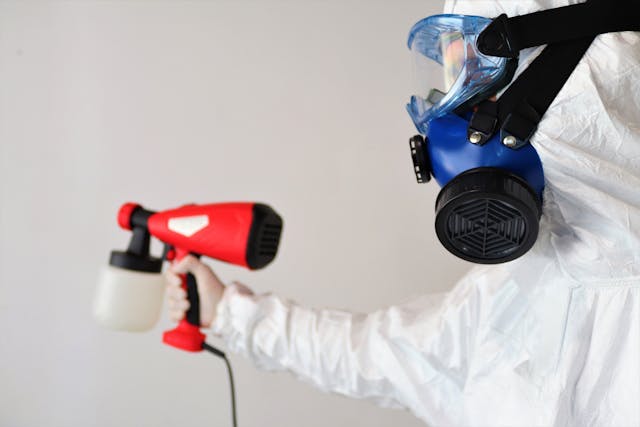 person in a hazmat suit spraying something on a white wall